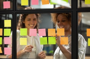 Happy diverse businesswomen laugh talk check project progress on stickers